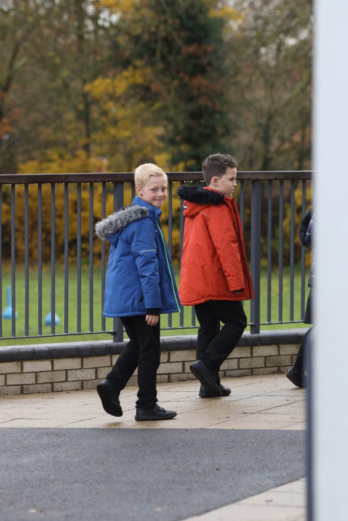 two pupils with coats on in the school grounds